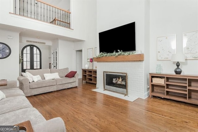 living room with hardwood / wood-style flooring, a towering ceiling, a fireplace, and french doors