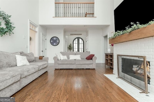 living room featuring a brick fireplace, wood-type flooring, and a high ceiling