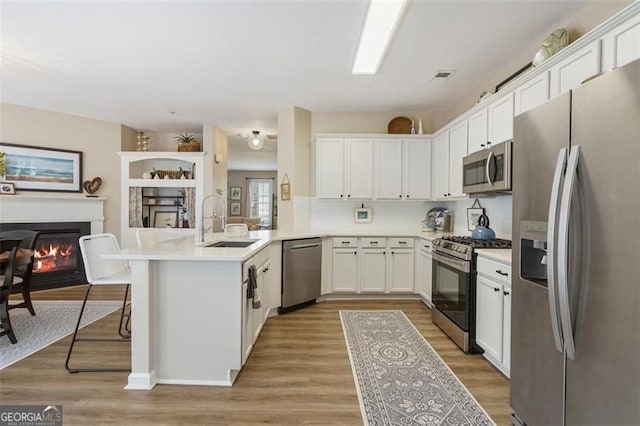 kitchen featuring a kitchen bar, sink, white cabinetry, appliances with stainless steel finishes, and kitchen peninsula