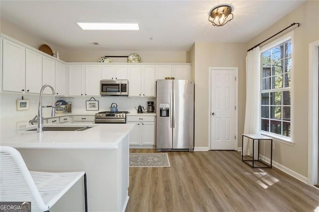 kitchen featuring sink, white cabinetry, appliances with stainless steel finishes, kitchen peninsula, and light hardwood / wood-style floors