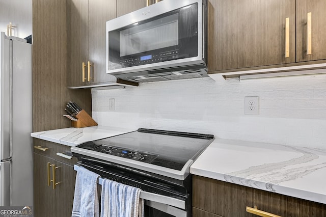 kitchen featuring light stone countertops, decorative backsplash, dark brown cabinets, and stainless steel appliances