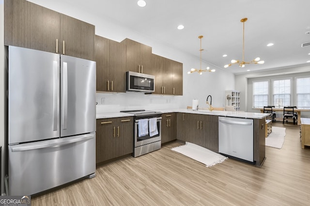 kitchen with pendant lighting, sink, appliances with stainless steel finishes, an inviting chandelier, and light wood-type flooring