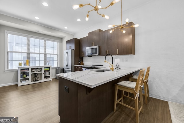 kitchen with sink, appliances with stainless steel finishes, light hardwood / wood-style floors, a kitchen bar, and kitchen peninsula