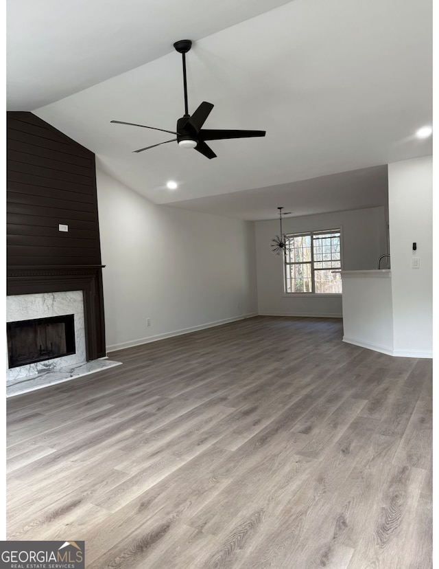 unfurnished living room featuring ceiling fan, lofted ceiling, a fireplace, and light hardwood / wood-style flooring