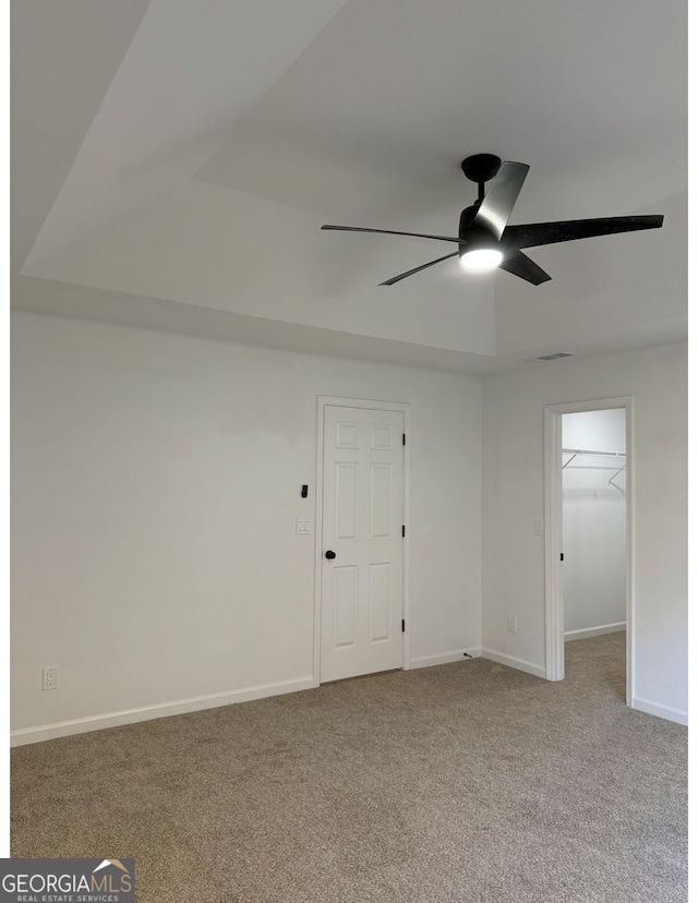 empty room with light carpet, ceiling fan, and a tray ceiling