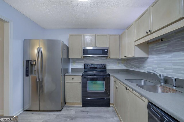 kitchen featuring a sink, light countertops, light wood-type flooring, decorative backsplash, and black appliances