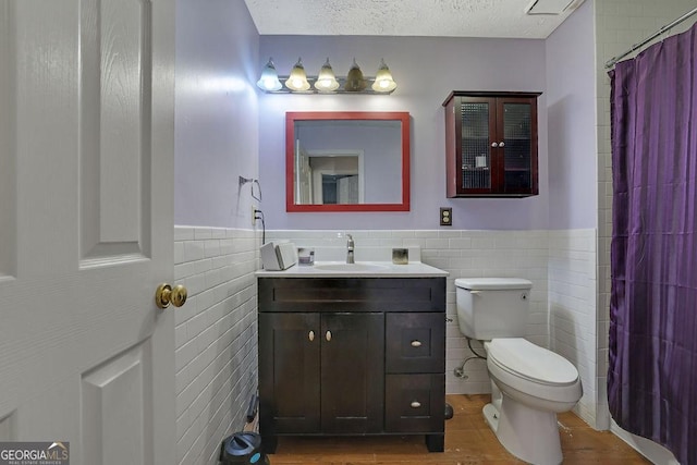 full bathroom with toilet, a wainscoted wall, a textured ceiling, and vanity