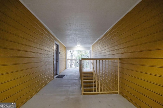 hall featuring concrete flooring, wood walls, and an upstairs landing