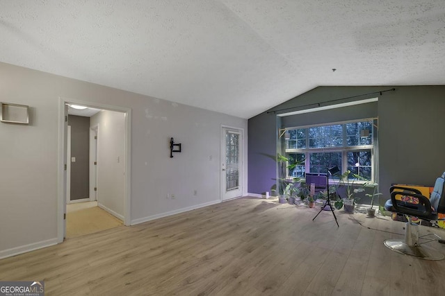 living room featuring lofted ceiling, baseboards, light wood-style flooring, and a textured ceiling