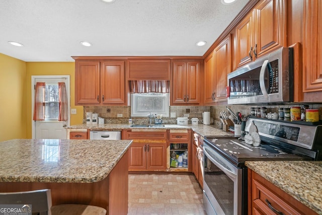 kitchen with a breakfast bar, sink, stainless steel appliances, light stone countertops, and backsplash