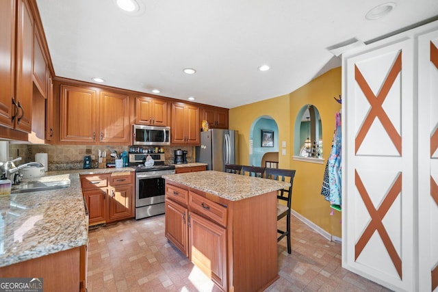 kitchen featuring sink, stainless steel appliances, a center island, light stone counters, and a kitchen bar