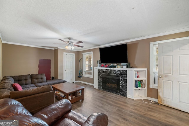 living room with crown molding, a textured ceiling, ceiling fan, a fireplace, and hardwood / wood-style floors