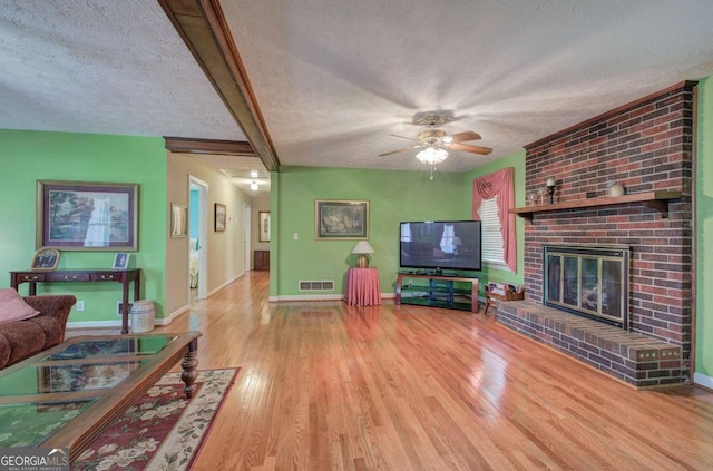 living room featuring a fireplace, beam ceiling, light hardwood / wood-style floors, and a textured ceiling