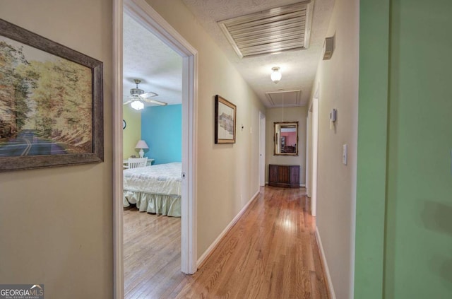 hall with a textured ceiling and light hardwood / wood-style flooring