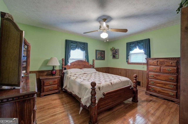 bedroom featuring wooden walls, a textured ceiling, ceiling fan, and light hardwood / wood-style floors