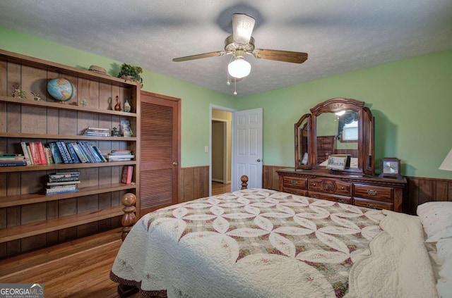 bedroom featuring ceiling fan, wood-type flooring, a textured ceiling, and wood walls