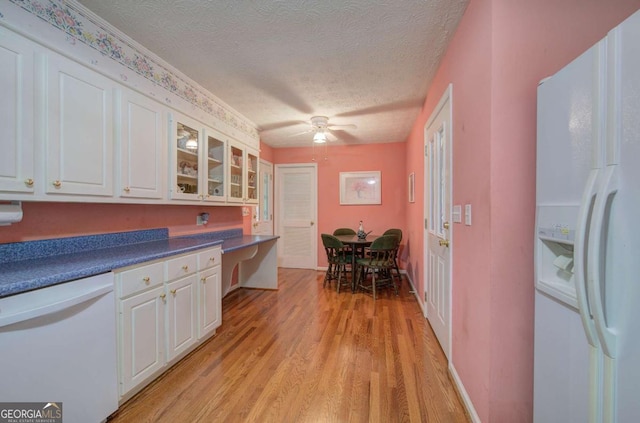 kitchen with white cabinetry, built in desk, a textured ceiling, light wood-type flooring, and white appliances