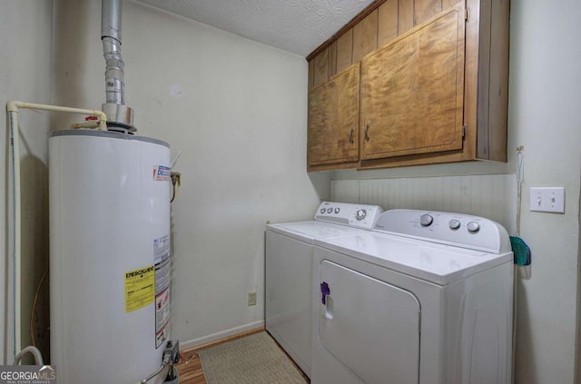 clothes washing area featuring cabinets, a textured ceiling, washer and dryer, and gas water heater