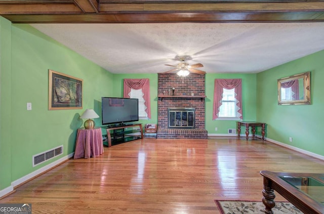 living room with ceiling fan, a brick fireplace, light wood-type flooring, and a textured ceiling