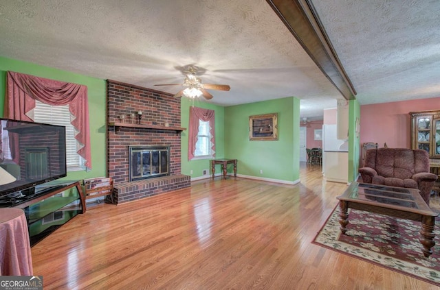 living room featuring ceiling fan, a fireplace, light hardwood / wood-style floors, and a textured ceiling