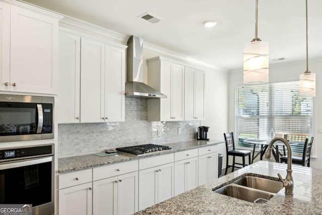 kitchen with pendant lighting, wall chimney range hood, sink, appliances with stainless steel finishes, and white cabinetry