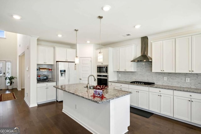 kitchen featuring light stone counters, appliances with stainless steel finishes, wall chimney exhaust hood, and a kitchen island with sink