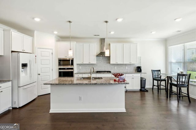 kitchen featuring appliances with stainless steel finishes, pendant lighting, an island with sink, sink, and wall chimney range hood