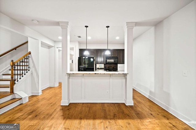 kitchen with pendant lighting, light hardwood / wood-style floors, black appliances, and decorative columns