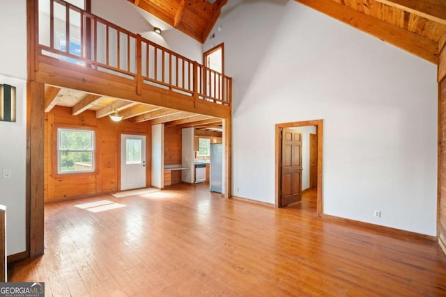 unfurnished living room with beam ceiling, high vaulted ceiling, wooden ceiling, and light hardwood / wood-style floors