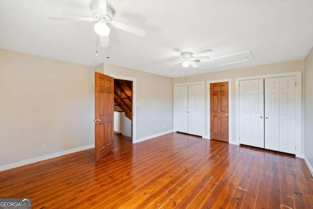 unfurnished bedroom featuring dark wood-type flooring, ceiling fan, and two closets