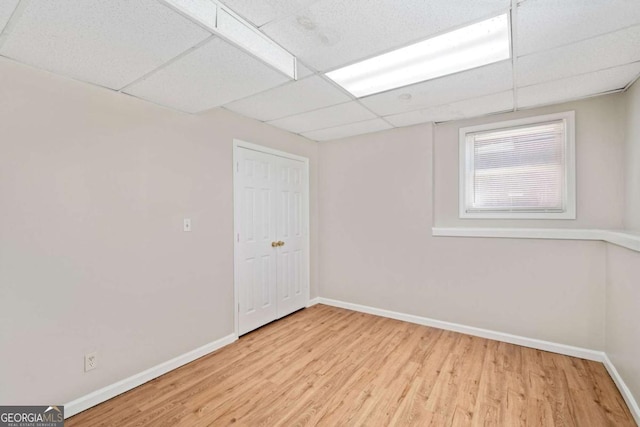 basement featuring a paneled ceiling and light hardwood / wood-style flooring