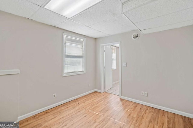 spare room featuring a drop ceiling and light hardwood / wood-style floors