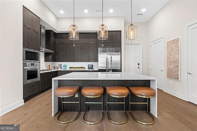 kitchen featuring built in appliances, a kitchen island with sink, and light hardwood / wood-style flooring