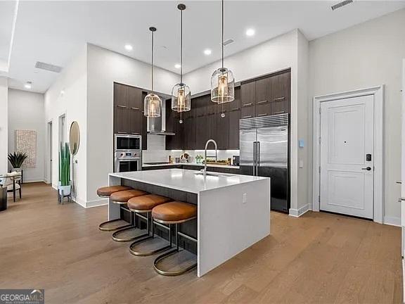 kitchen with a breakfast bar area, built in appliances, hanging light fixtures, dark brown cabinets, and a center island with sink