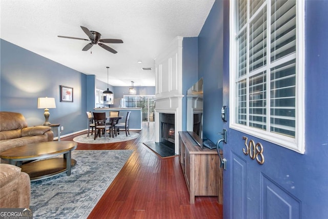 living room with dark hardwood / wood-style flooring, ceiling fan, and a textured ceiling