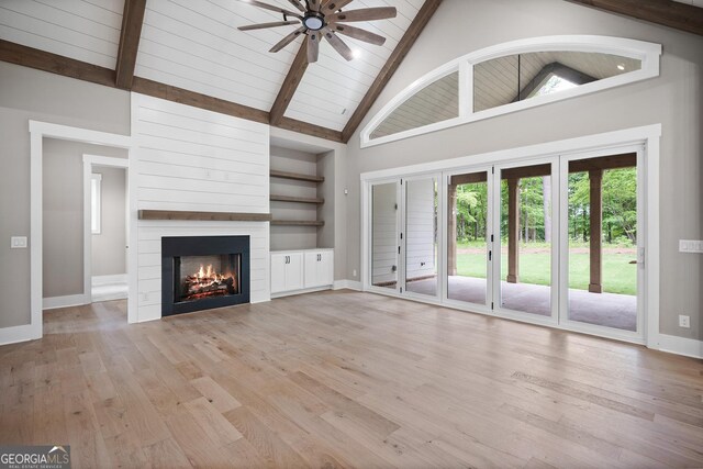 unfurnished living room featuring ceiling fan with notable chandelier, a large fireplace, high vaulted ceiling, and light wood-type flooring