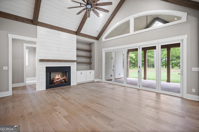 unfurnished living room featuring a large fireplace, beamed ceiling, light wood-type flooring, and baseboards