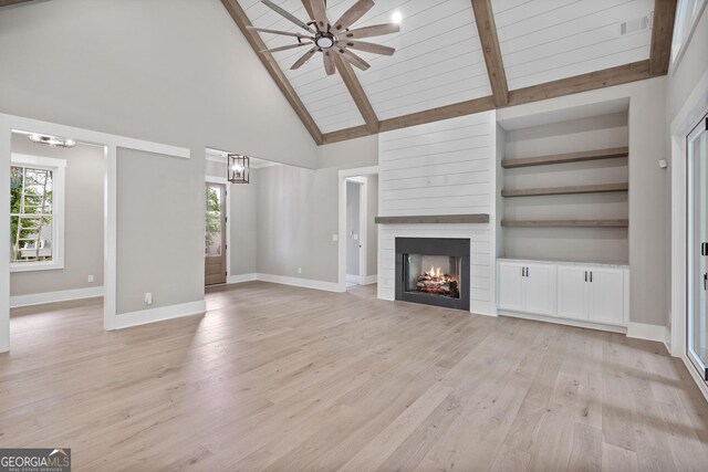 unfurnished living room with a fireplace, light wood-type flooring, built in features, beam ceiling, and ceiling fan with notable chandelier