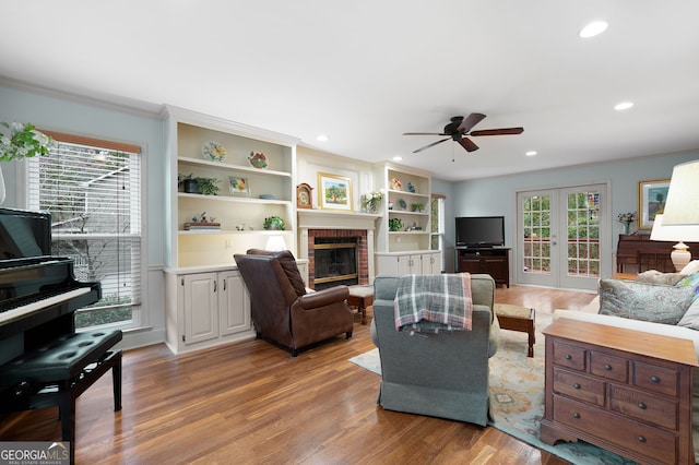 living room featuring crown molding, a wealth of natural light, a brick fireplace, and light wood-type flooring