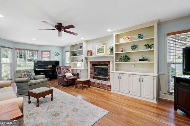 living room with built in features, a healthy amount of sunlight, a brick fireplace, and light hardwood / wood-style flooring