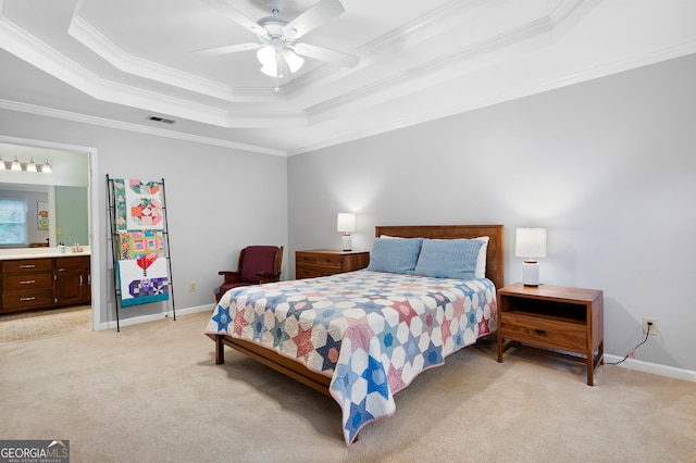 bedroom featuring ornamental molding, light colored carpet, ceiling fan, a tray ceiling, and ensuite bath