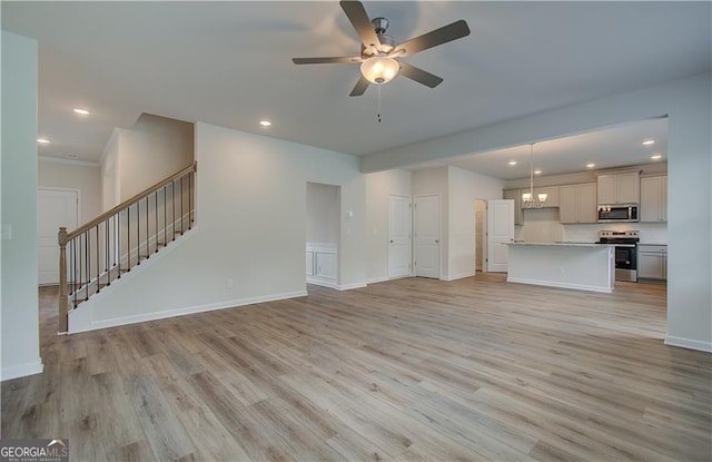 unfurnished living room featuring ceiling fan with notable chandelier and light hardwood / wood-style flooring