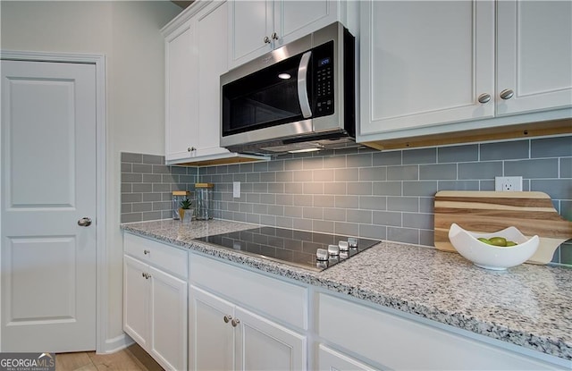 kitchen featuring white cabinetry, light stone countertops, black electric cooktop, and decorative backsplash