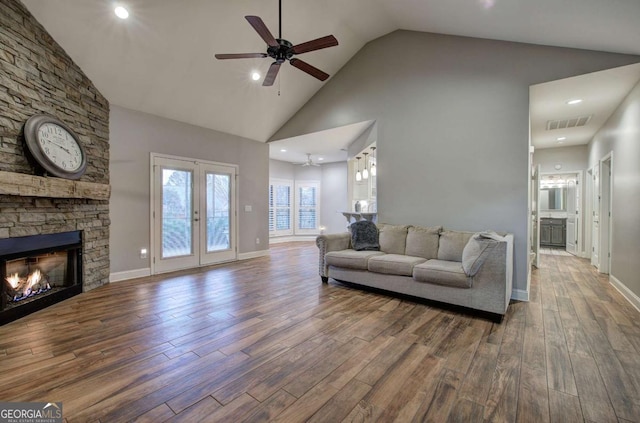 living room with a stone fireplace, high vaulted ceiling, hardwood / wood-style flooring, ceiling fan, and french doors