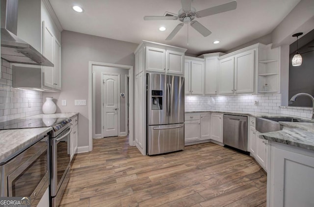 kitchen featuring sink, appliances with stainless steel finishes, white cabinetry, light stone counters, and wall chimney exhaust hood