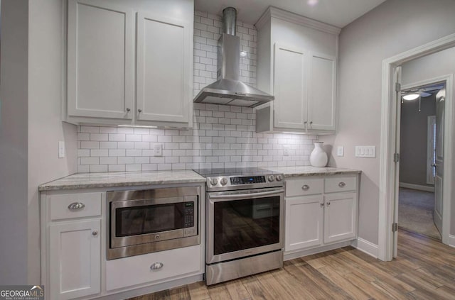 kitchen with light stone counters, appliances with stainless steel finishes, wall chimney exhaust hood, and white cabinets