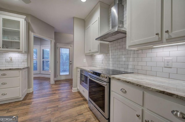 kitchen with tasteful backsplash, appliances with stainless steel finishes, hardwood / wood-style flooring, wall chimney range hood, and white cabinets