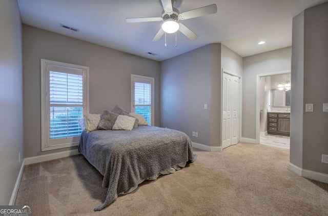 bedroom with light carpet, ensuite bath, a closet, and ceiling fan