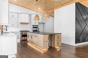 kitchen with pendant lighting, an island with sink, sink, white cabinets, and high end range