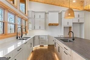 kitchen with white cabinetry, sink, hanging light fixtures, and stone counters